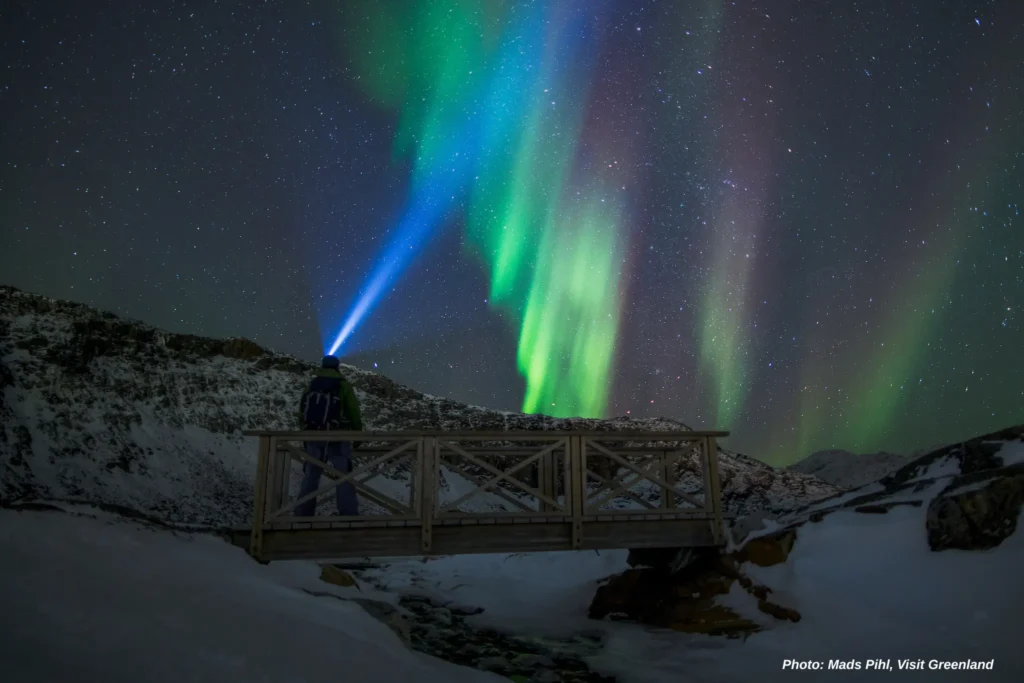 A hiker near Nuuk looking up at the autumn northern lights in Greenland