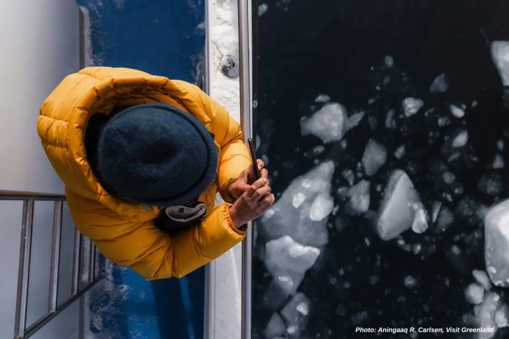 A woman with yellow jacket photographing ice floes below - Photo by Aningaaq R. Carlsen - Visit Greenland